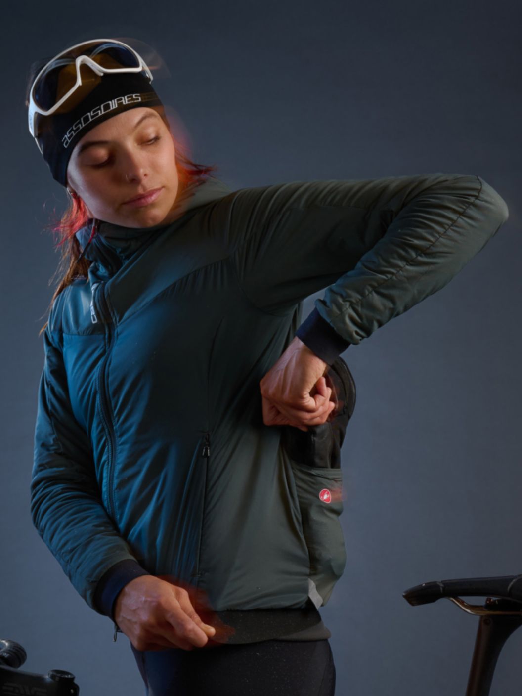 A glowy and slightly motion-blurred image of a road rider in heavy winter apparel standing while reaching for an additional clothing layer from their jacket pocket. 